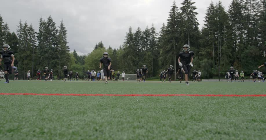A youth football team is running drills on a field during the day