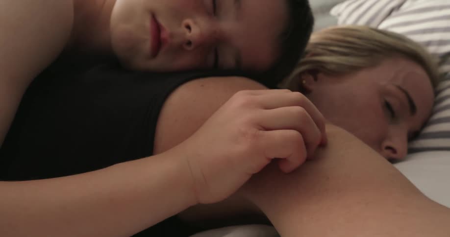 A son rests on his mothers back in bed during the daytime gently caressing her shoulder in a tender peaceful moment