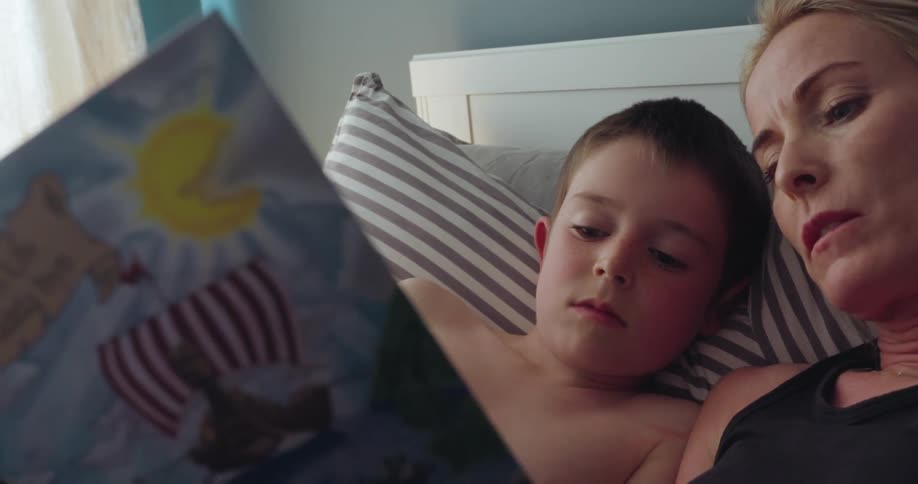 Woman reads a book to her child inside the bedroom in the morning