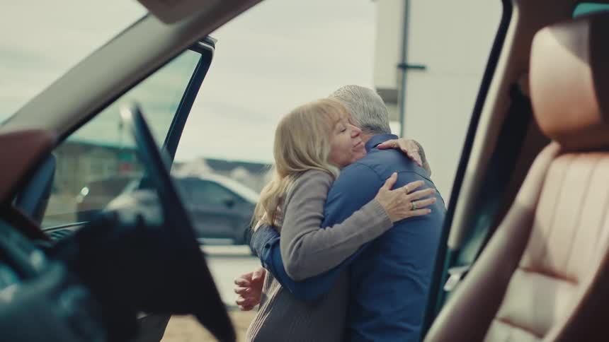 A husband and wife hug before the man gets in the car
