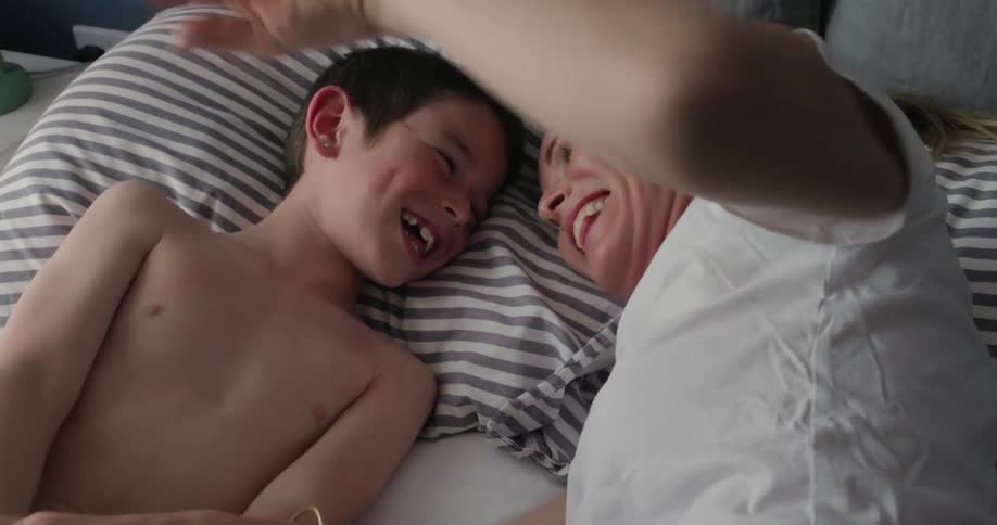 Mother lying down with her son playing in bed