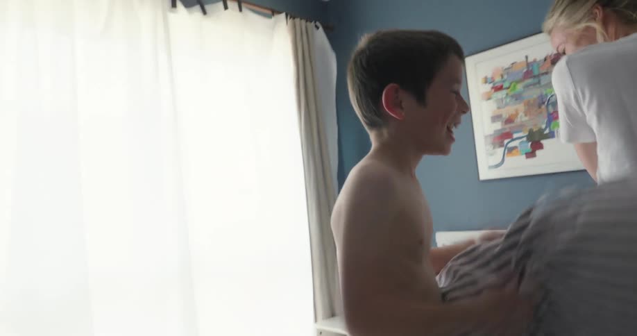 Mother and son hits each other with pillows on the bed at daytime