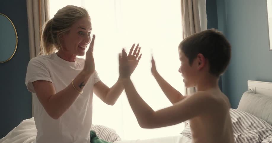 Mother and son sitting on the bed playing patty cakes in the morning
