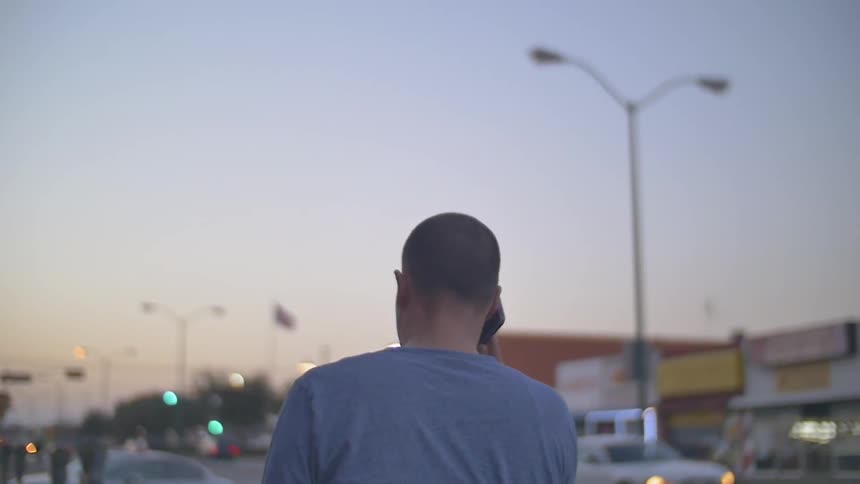 Man walks down city street at dusk while on the phone