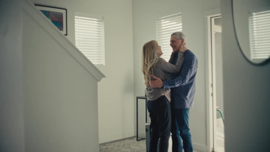 A couple embraces warmly in the entryway of a home smiling and sharing an intimate moment