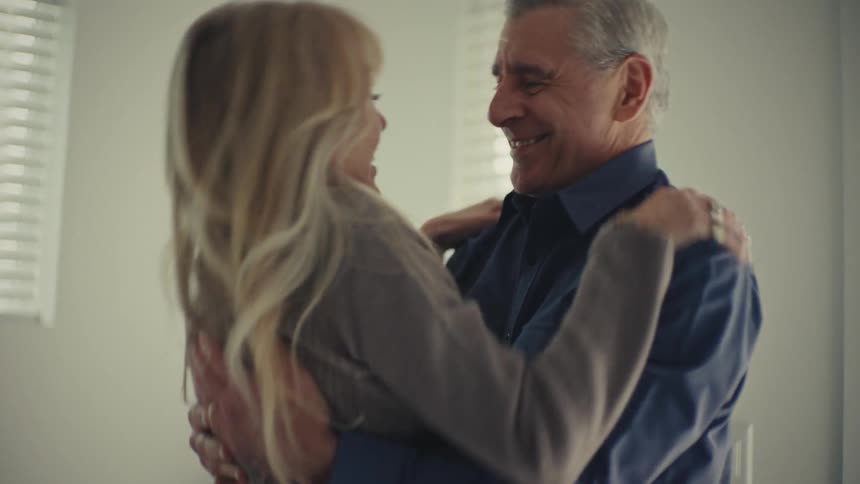 Man and woman embrace each other warmly in a bright domestic setting