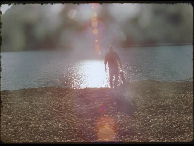 Person holding a guitar walks along the seashore under intense sunlight