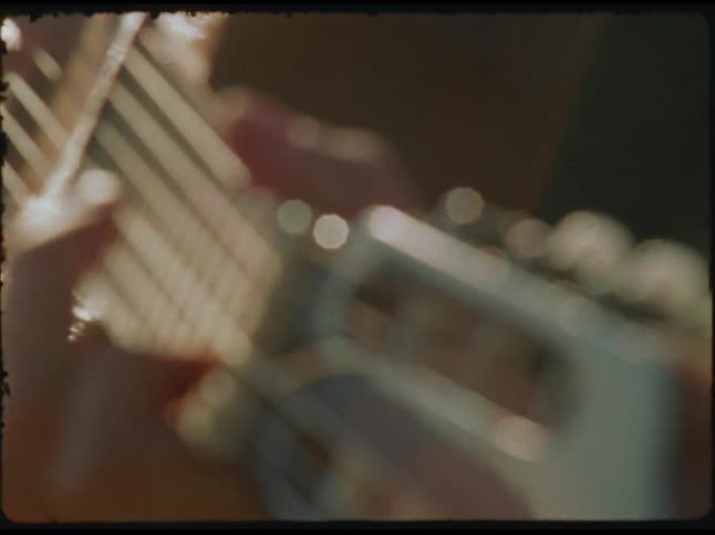 Hands gently pluck the strings of a guitar in soft sunlight