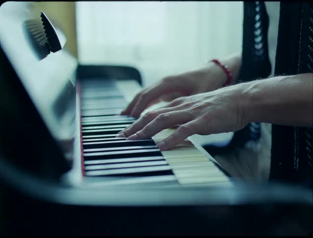 A closeup shot of a persons hands playing an upright piano in soft natural daylight