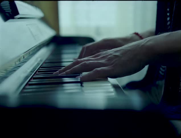 Man plays a piano standing near a curtained window during the daytime