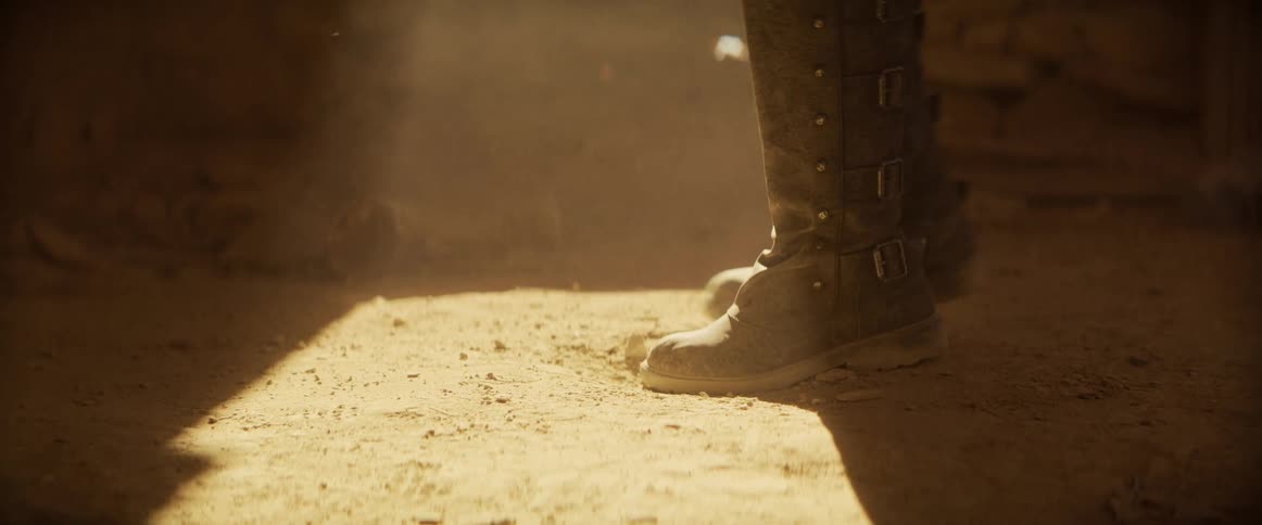 A person wearing tall leather boots arriving and stopping in a place with sand and rocks with sunlight shining in the middle