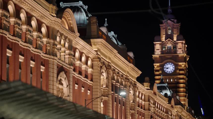 A clock tower stands above a large brick and stone building at night
