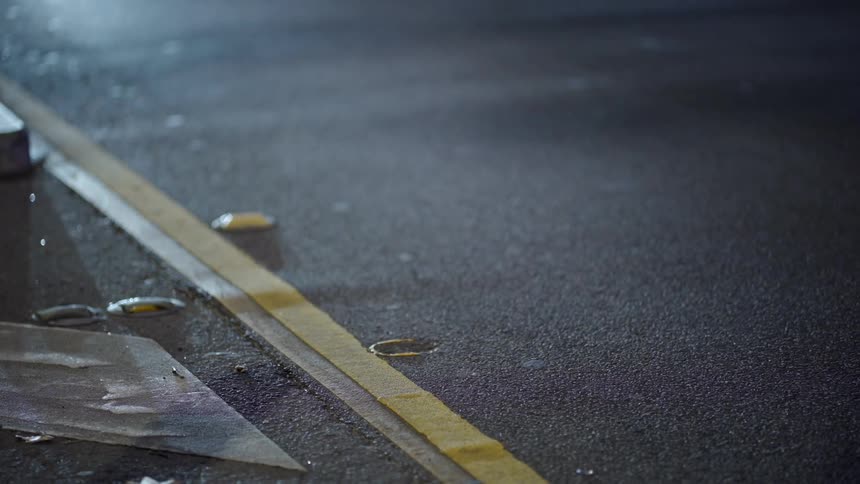 A white car drives past a yellow line on a dimly lit urban street at night