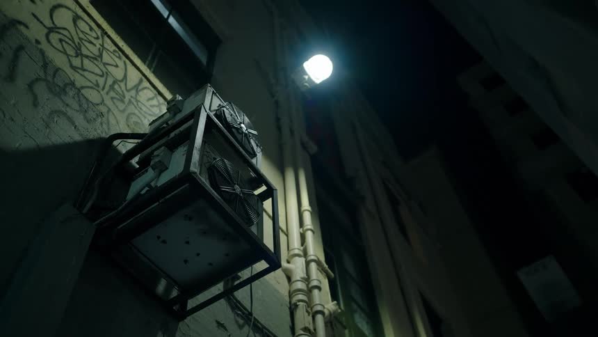 Outdoor building light illuminates graffiti and a frame holding outdoor ac units at night