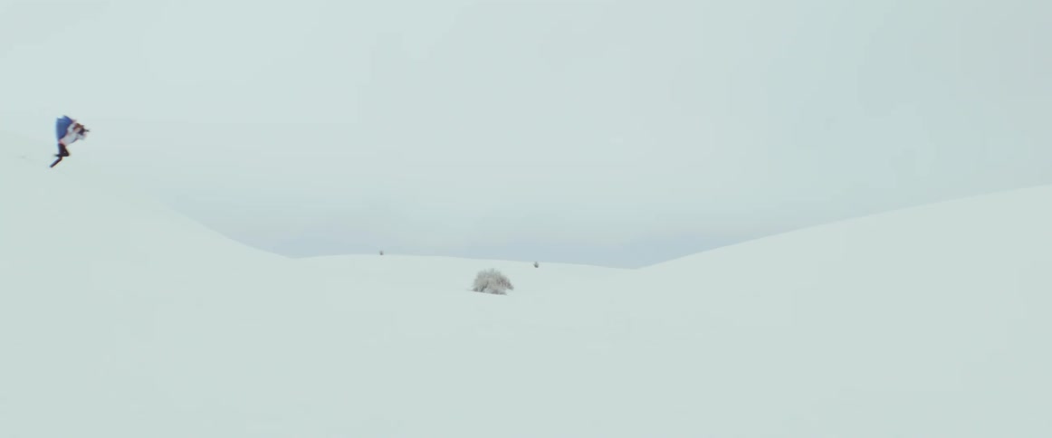 A person dashes down a snowy hill gripping a billowing blue blanket as it flutters in the wind