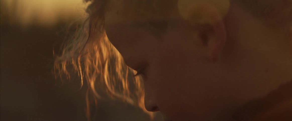A closeup of a childs face with short hair at the back and long strands framing the front illuminated by sunlight in a desert at sunrise or sunset