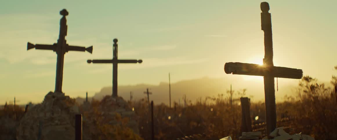 Three crosses stand in a field at sunset surrounded by dry vegetation and rocks