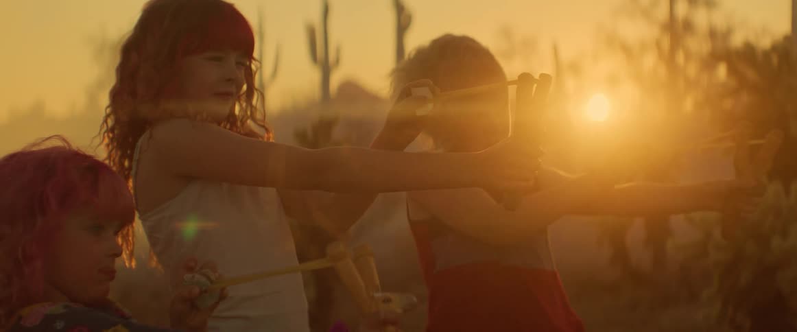 A group of girls is practicing with slingshots in a desertlike landscape as the sun sets