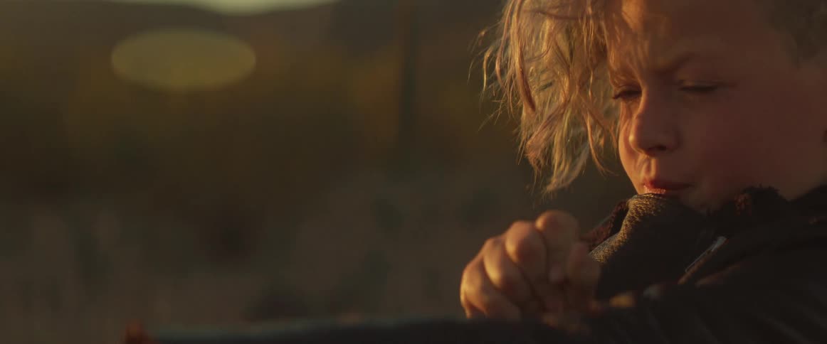 A determined child aims a slingshot with intense focus in golden sunset light