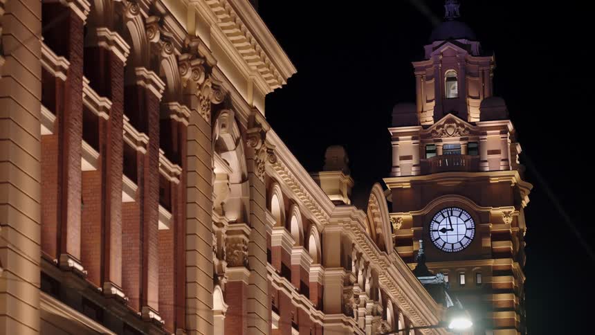 An ornate clock tower with a lit face rises beside a detailed building facade under the night sky