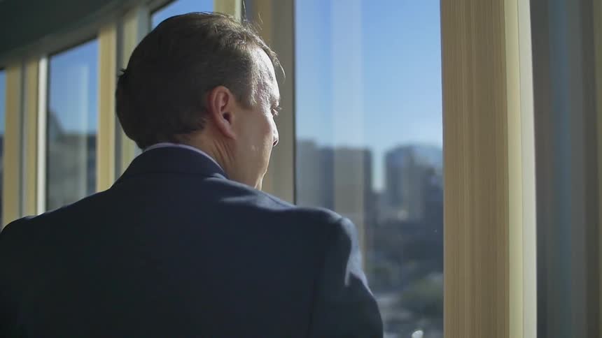 A man is walking past large windows overseeing a city