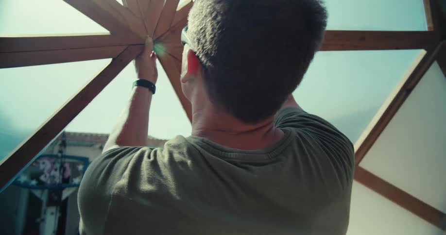 A person wearing sunglasses is working on the construction of a geodesic dome structure adjusting the plastic covering at the top