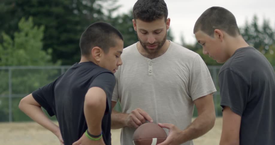 A man holds a football and instructs kids on what to do
