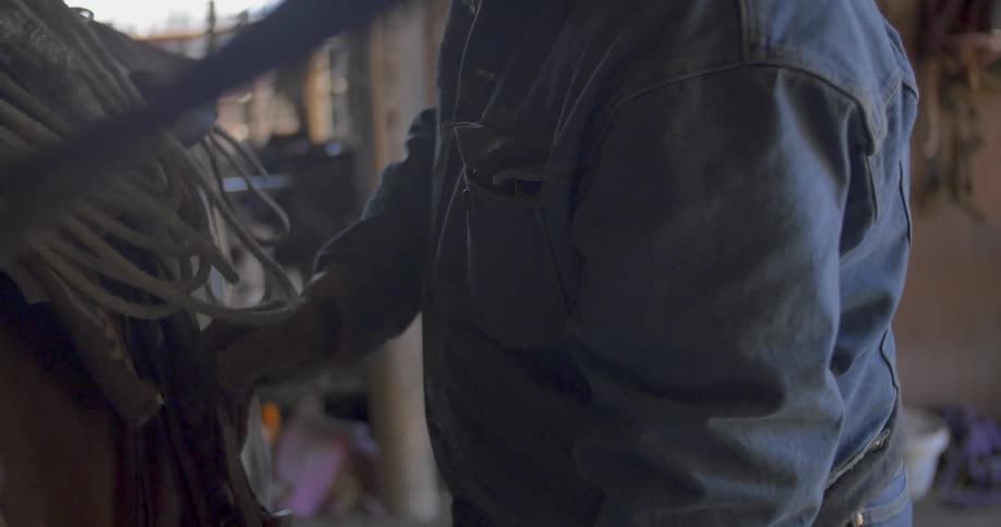 A cowboy ties a saddle to a horse