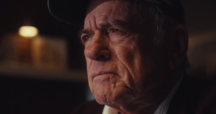 Elderly man frowns and sits back while watching his computer screen at night