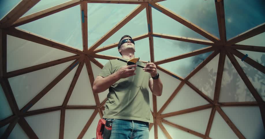 Man uses a clamp while constructing a domed building in a backyard on a summer day