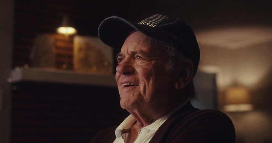 A closeup of an elderly man wearing a hat his expression thoughtful and content as he sits in a softly lit room