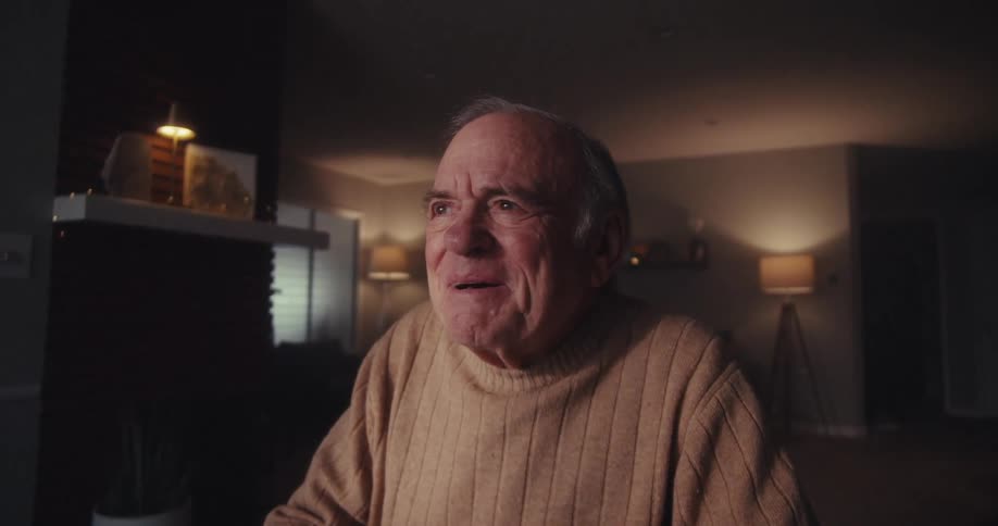 Elderly man smiles while watching his computer screen at home at night