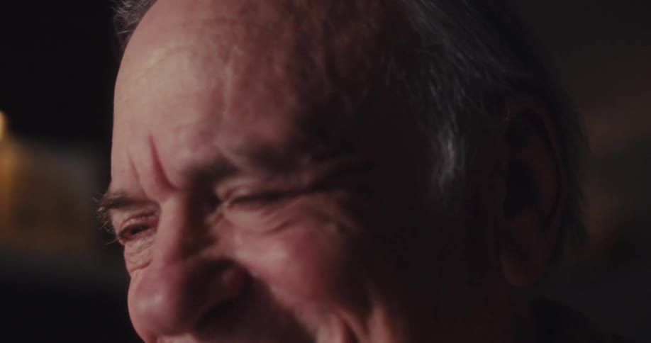 Elderly man laughs while sitting at home and enjoying amusing media