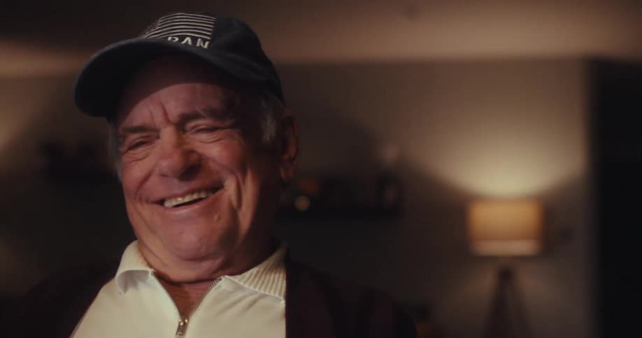 Elderly man sitting at home at night laughs while watching his computer screen