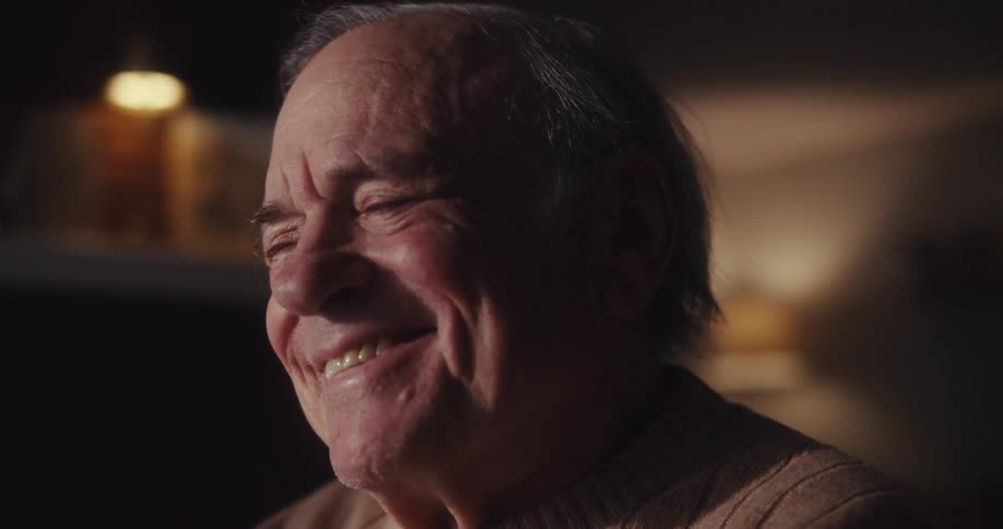 Elderly man laughs while watching a screen at home at night