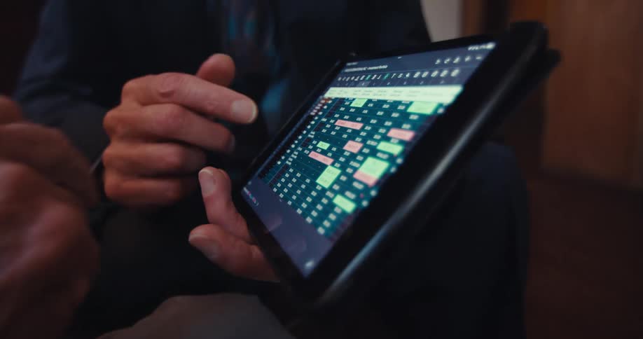 A man in a suit shows an elderly man an advertisement on a tablet pc as they both sit in the living room