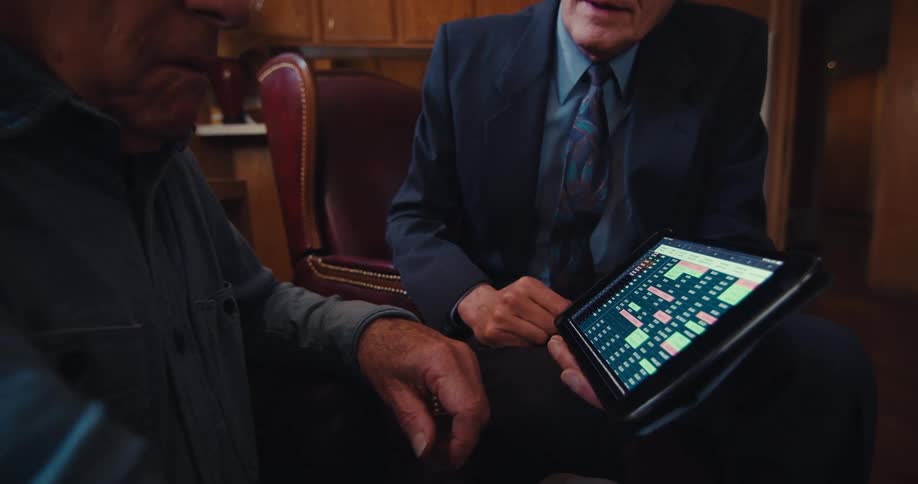 Businessman references a tablet during a discussion with an elderly male clientin the living room