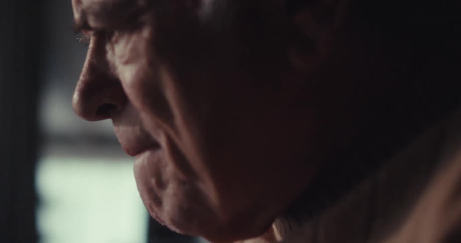 An elderly man sits alone in his living room looking really sad