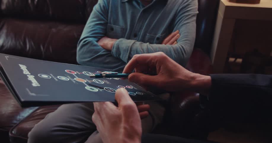 Two individuals are reviewing a trading strategy flowchart printed on a black surface with one person pointing at a central node with a pen