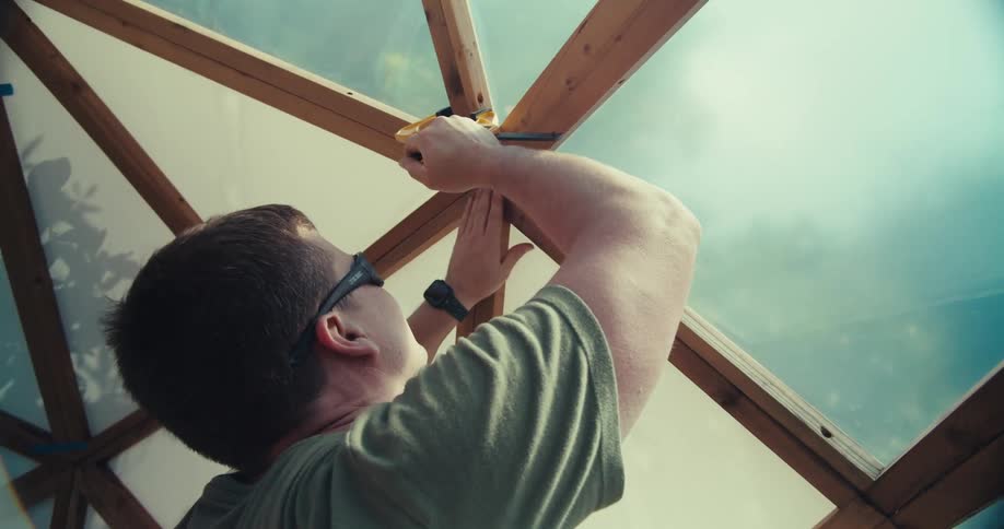 Man building a geometric dome uses a clamp to hold a joint together