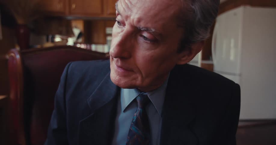 A person in a suit and tie sits in a room furnished with wooden cabinets explaining a financial chart to someone