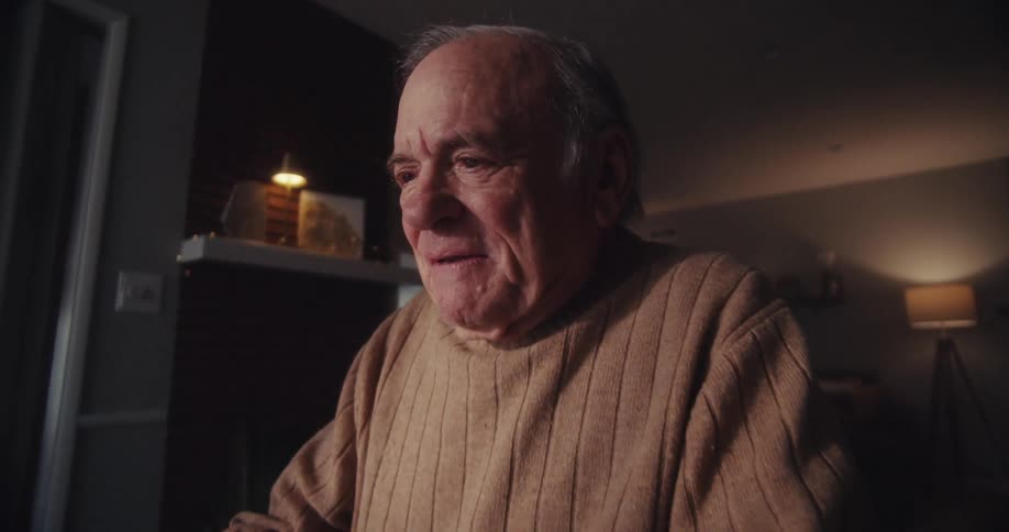 An elderly man appears happy after reading something on his laptop screen while sitting in his living room