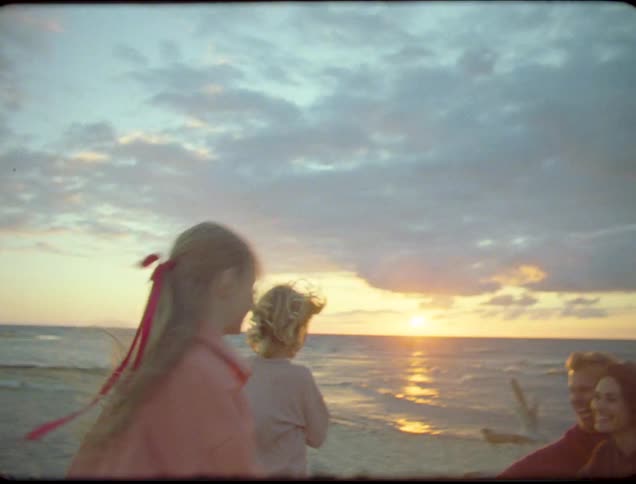 Three children running toward a woman and a man on the beach
