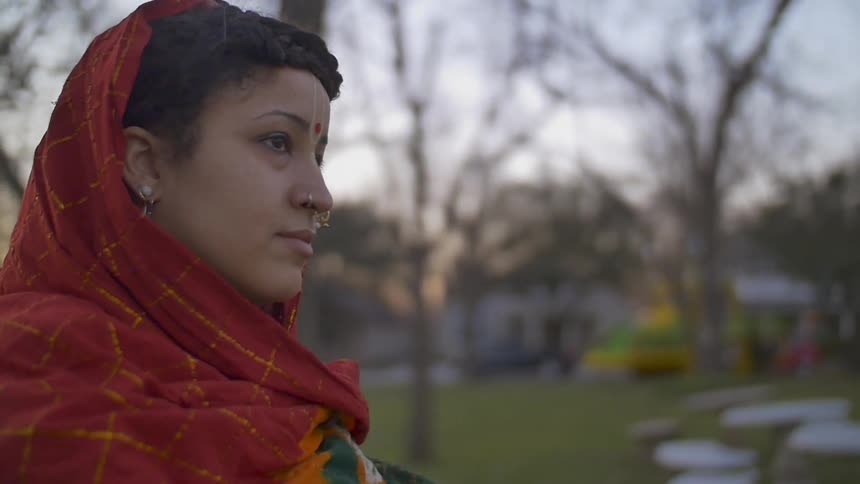 A woman in a red and gold scarf walks outside