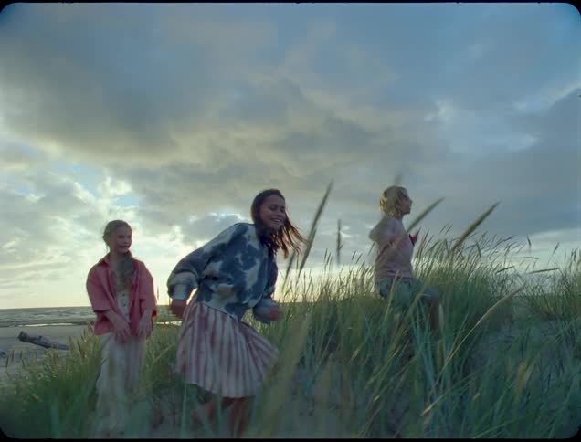 Kids run and play on the beach on a windy and cloudy day while the sun sits near the horizon