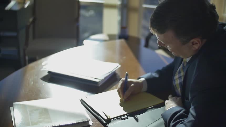 A man is sitting at a table writing on a pad