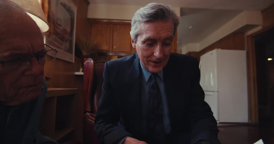 A man in a business suit sits in a living room carefully explaining documents to an elderly man