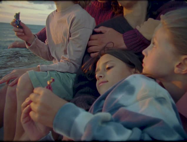 A family sit closely together seemingly enjoying the sunset over the ocean