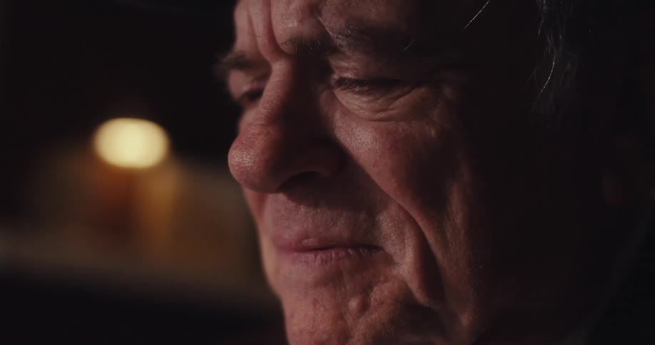 An elderly man looks sad as he types on his laptop computer indoors