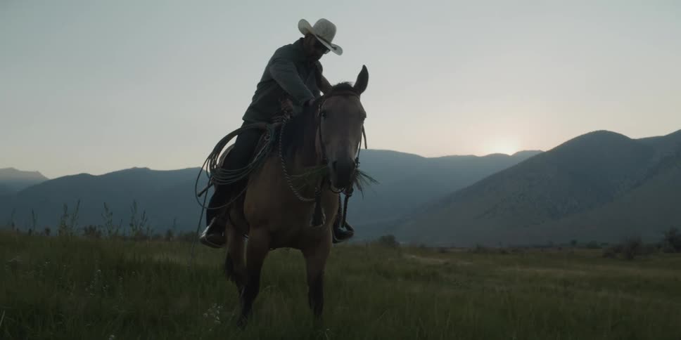 Man riding a horse in a field with mountains in the background
